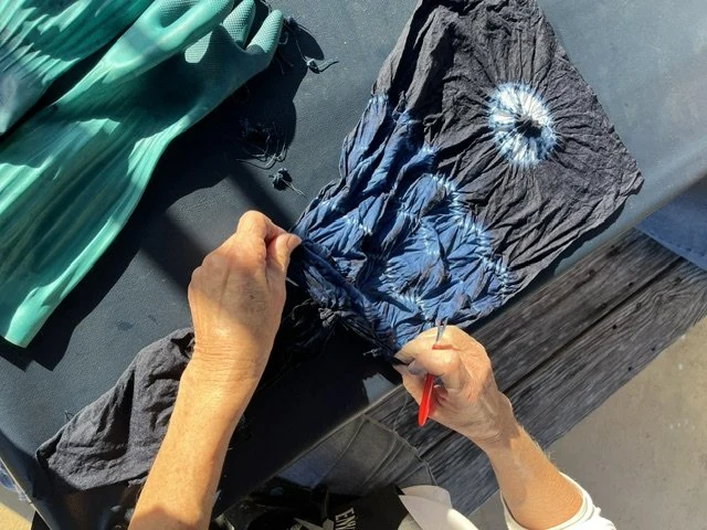 Hands snipping the threads to open a bound piece of indigo shibori